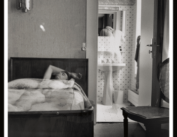 A black and white photograph showing a person lying on a bed in the foreground and another person leaning over a sink in a separate room. The image is titled "Room 7609, 1990" by Todd G. Franson.